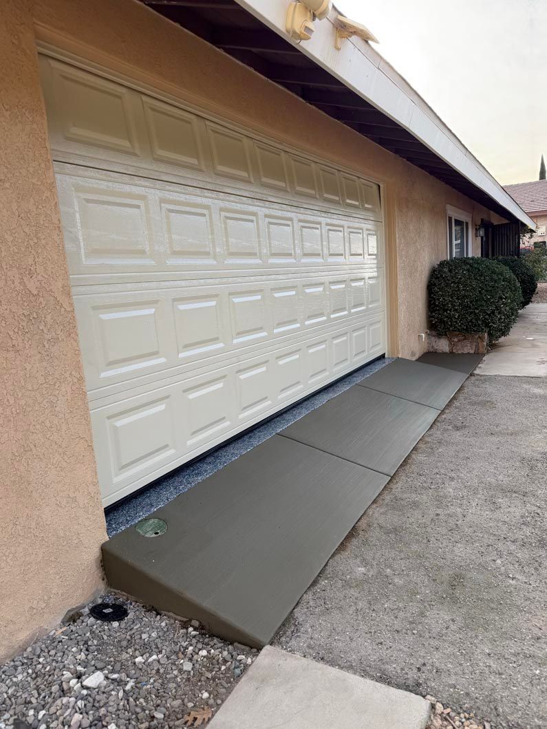 Residential garage with white door and a sloped concrete ramp leading to the driveway.
