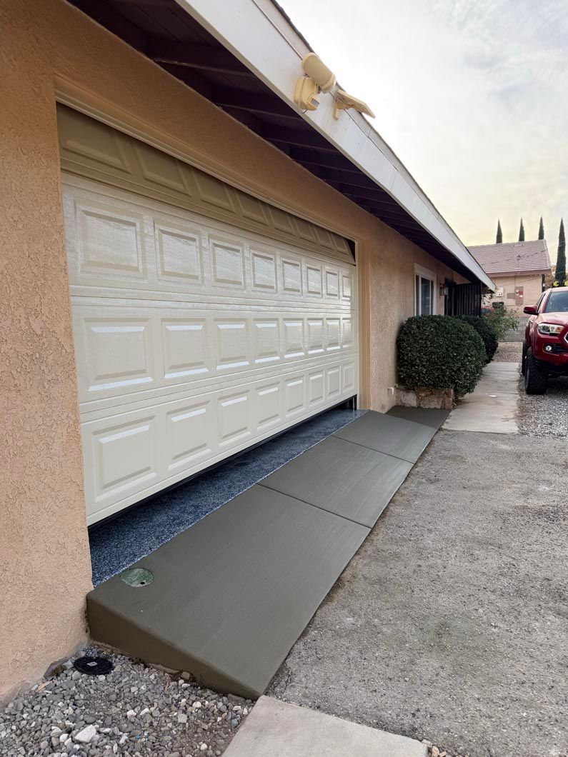 Garage with a sloped metal wheelchair ramp beside the driveway and a white garage door
