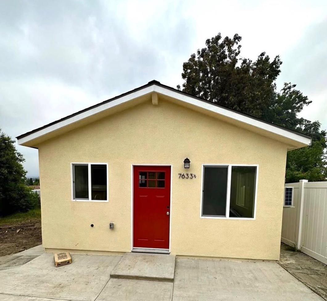 Small beige house with a red front door, white-trimmed windows, and a concrete driveway.