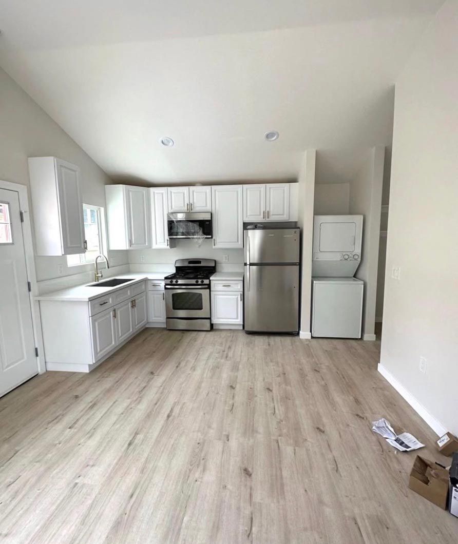 Bright empty kitchen with white cabinets, stainless steel appliances, and light wood flooring