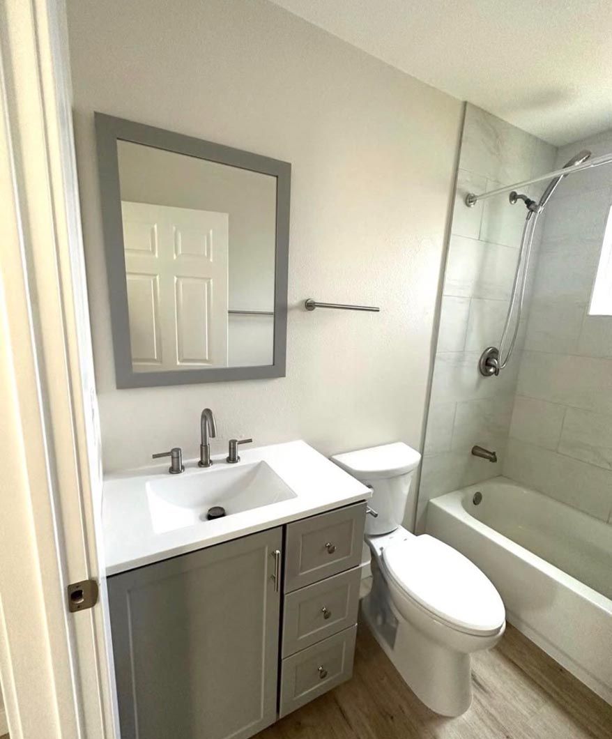 Small bathroom with gray vanity, toilet, bathtub, and a windowed shower area