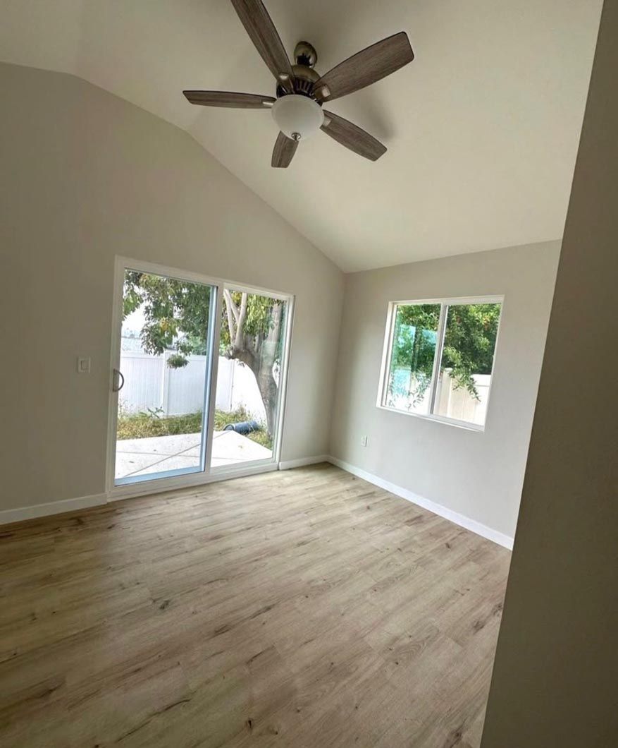 Empty room with light wood floors, white walls, ceiling fan, and sliding glass door to a patio.