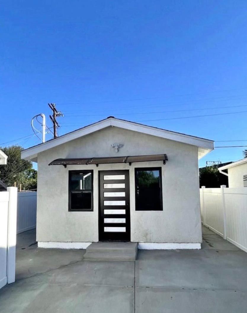Small white house with a black front door and driveway under a clear blue sky.