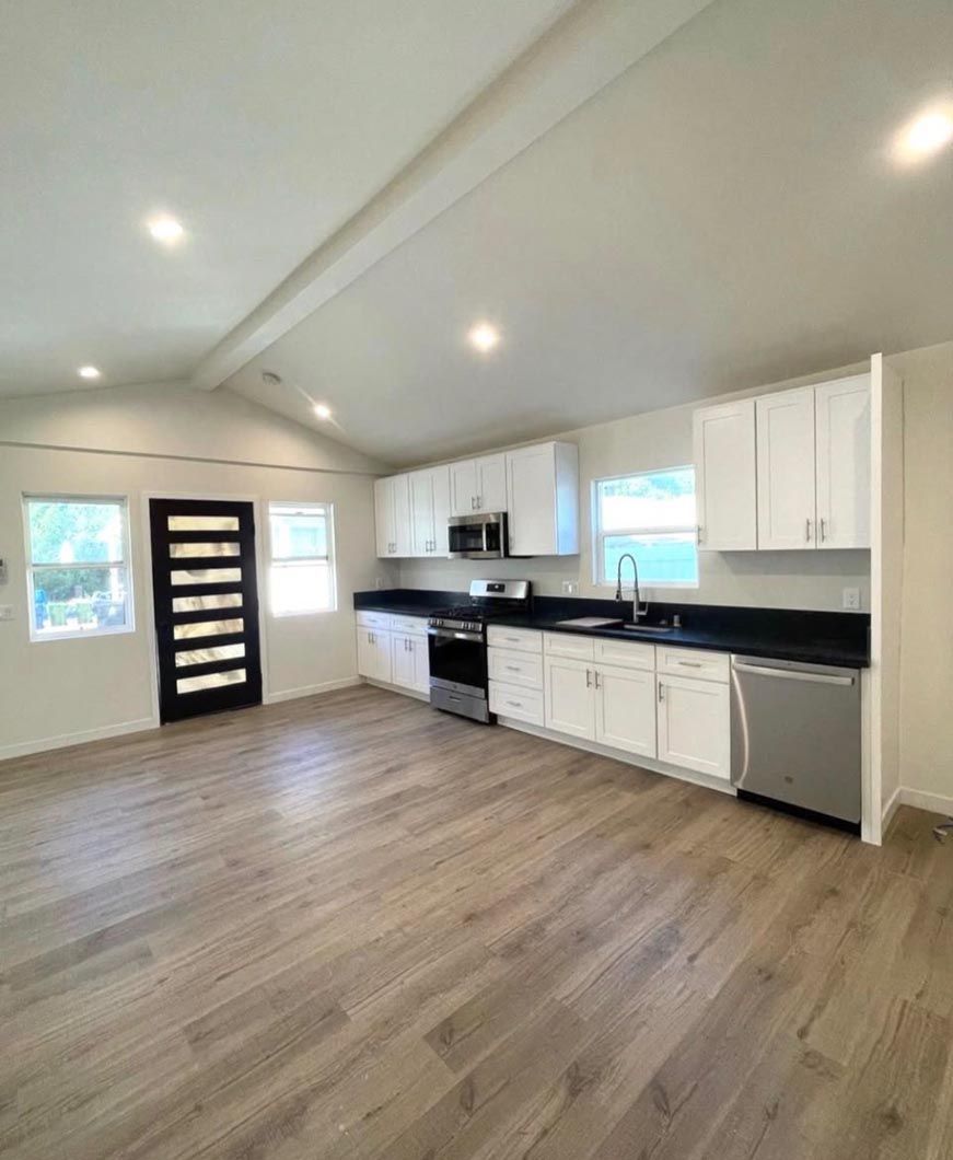Bright modern kitchen with white cabinets, black countertops, and wood-look flooring in an open room.