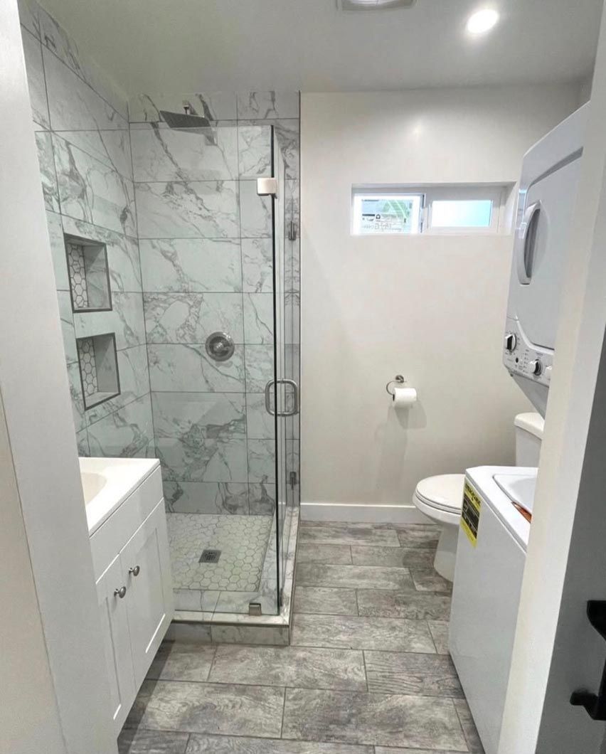 Modern bathroom with glass shower, white vanity, toilet, and stacked washer and dryer.