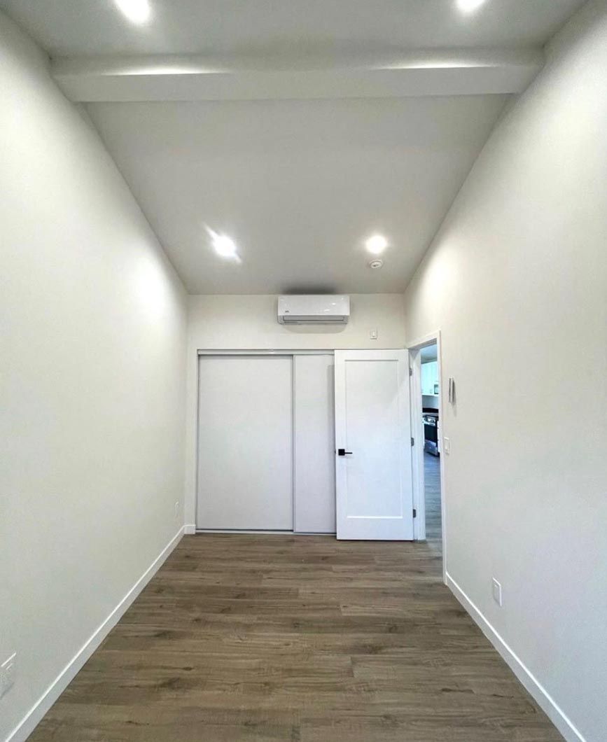 Narrow white hallway with wood floor, recessed lights, and a door at the end.