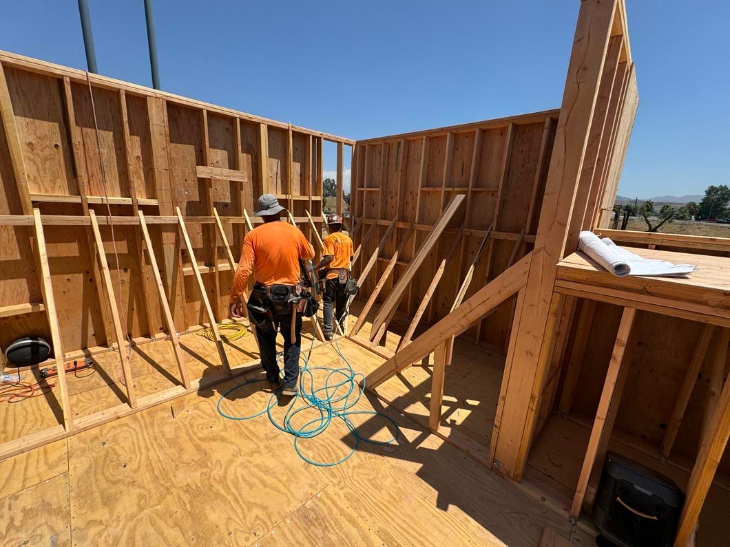 Construction workers framing wooden walls on a house under clear blue sky