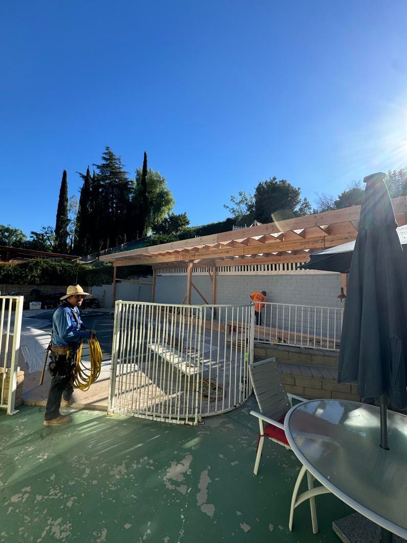Person walking through a white gate in a sunny backyard with a patio and house in the background