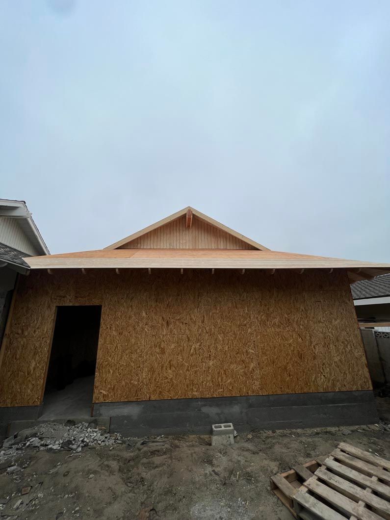 Partially built house with unfinished wooden walls and a metal roof under a cloudy sky