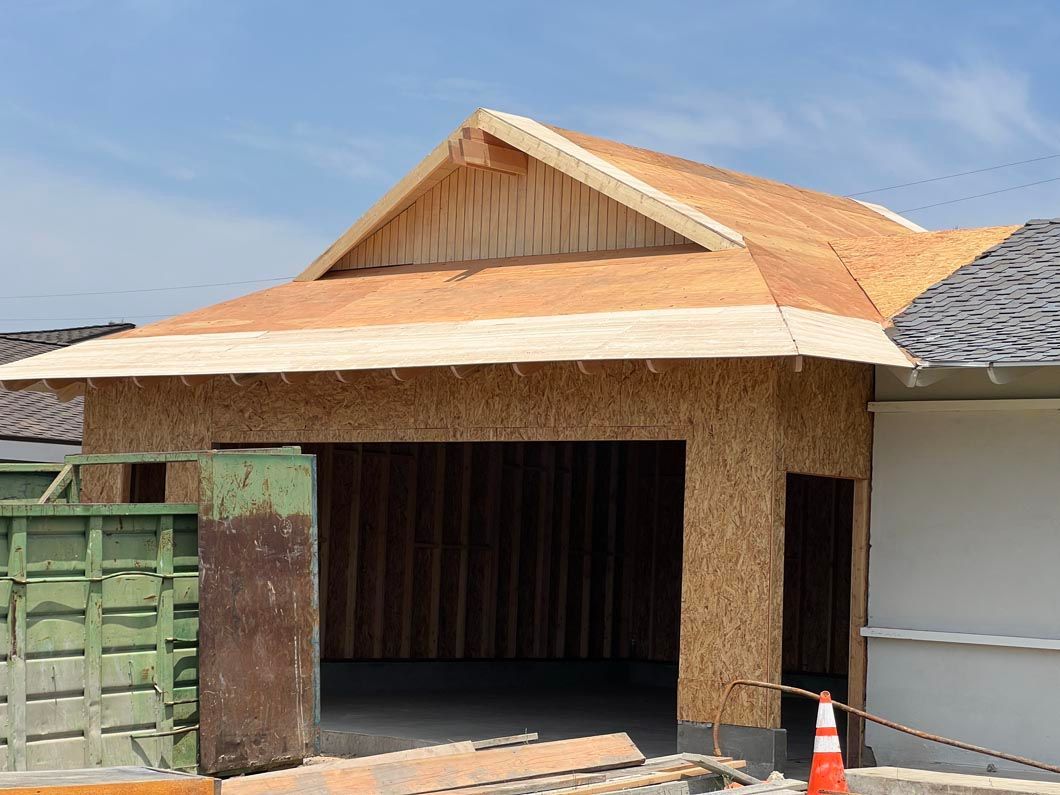 Small house under construction with a tiled roof, open garage-like entrance, and a traffic cone nearby.