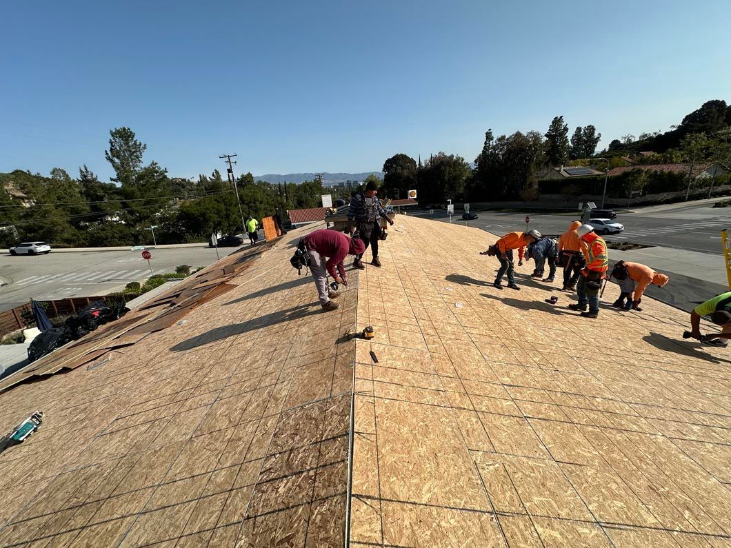 Workers installing shingles on a roof, with tools and materials spread across the surface.