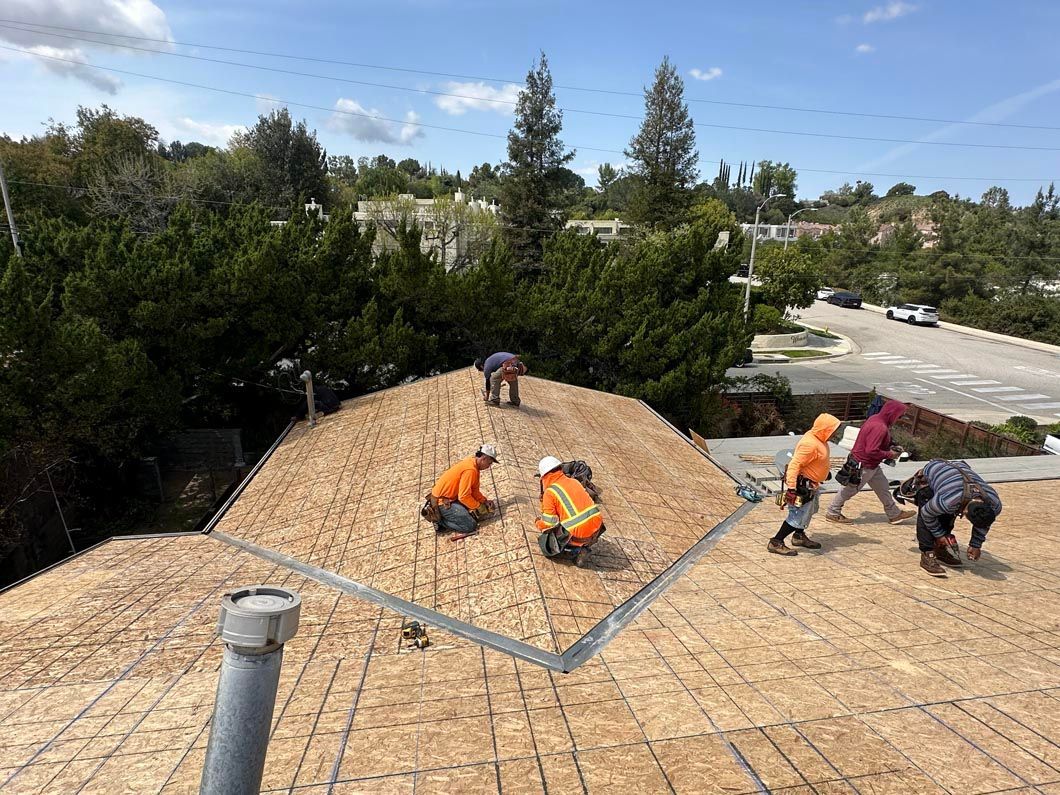 Workers installing roofing on a shingled roof under a blue sky.