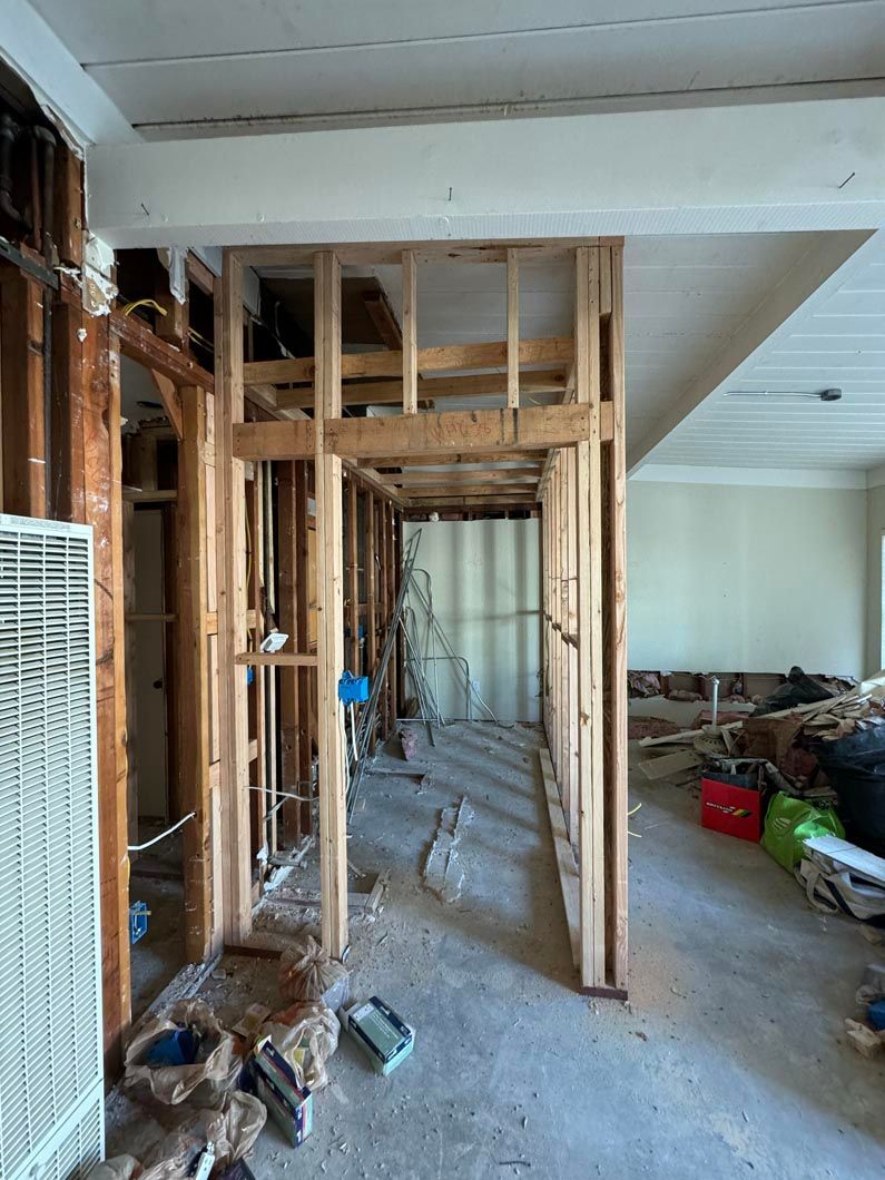 Exposed wooden framing in a room under renovation, with debris on the floor and a hallway beyond.