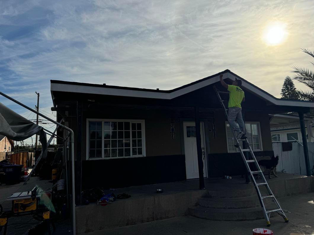 Person on a ladder painting the roof of a small house at sunset.