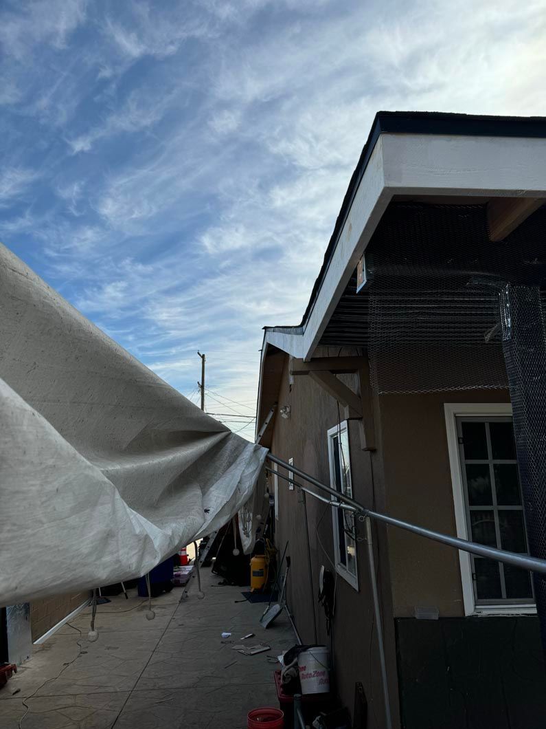 Narrow alley beside brown house with white tarp overhead under a cloudy blue sky