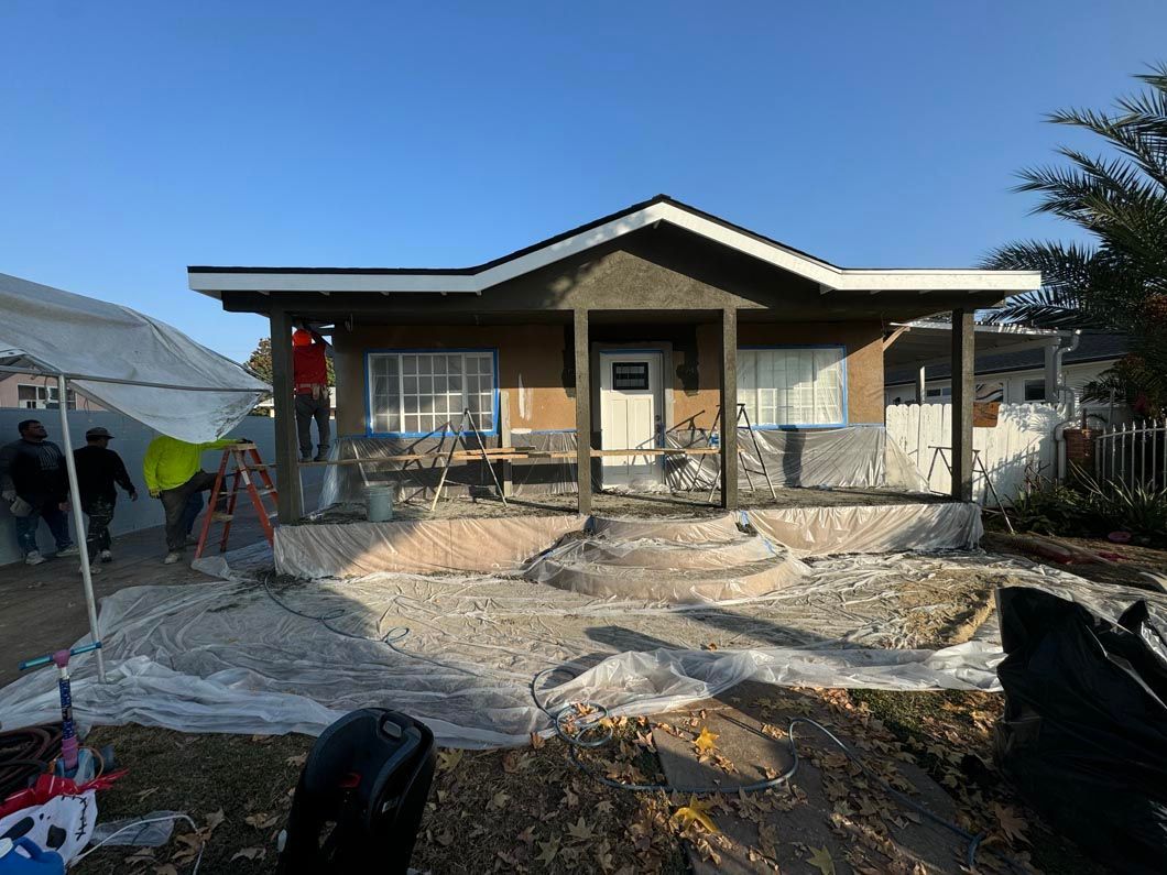 Single-story house under construction with workers and gravel yard in front