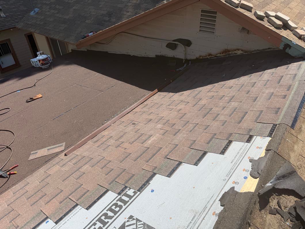 Partially repaired shingle roof with exposed underlayment and roofing materials on a house