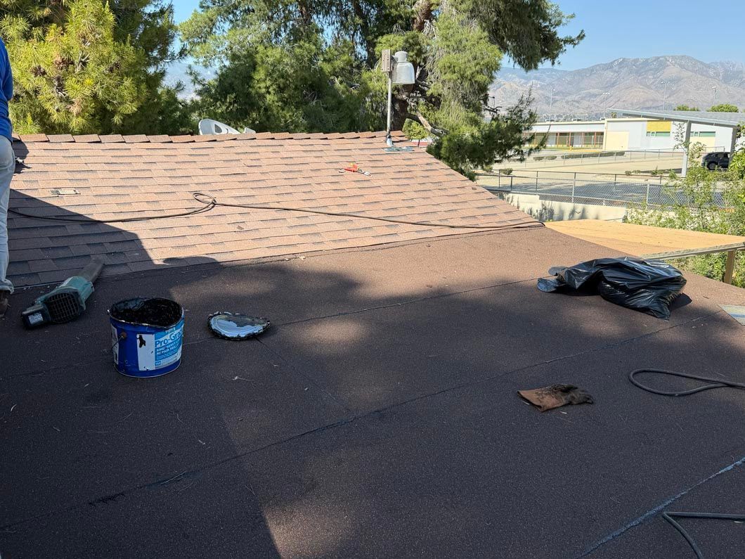 Flat rooftop with scattered tools and debris, backed by trees and distant mountains under a clear sky