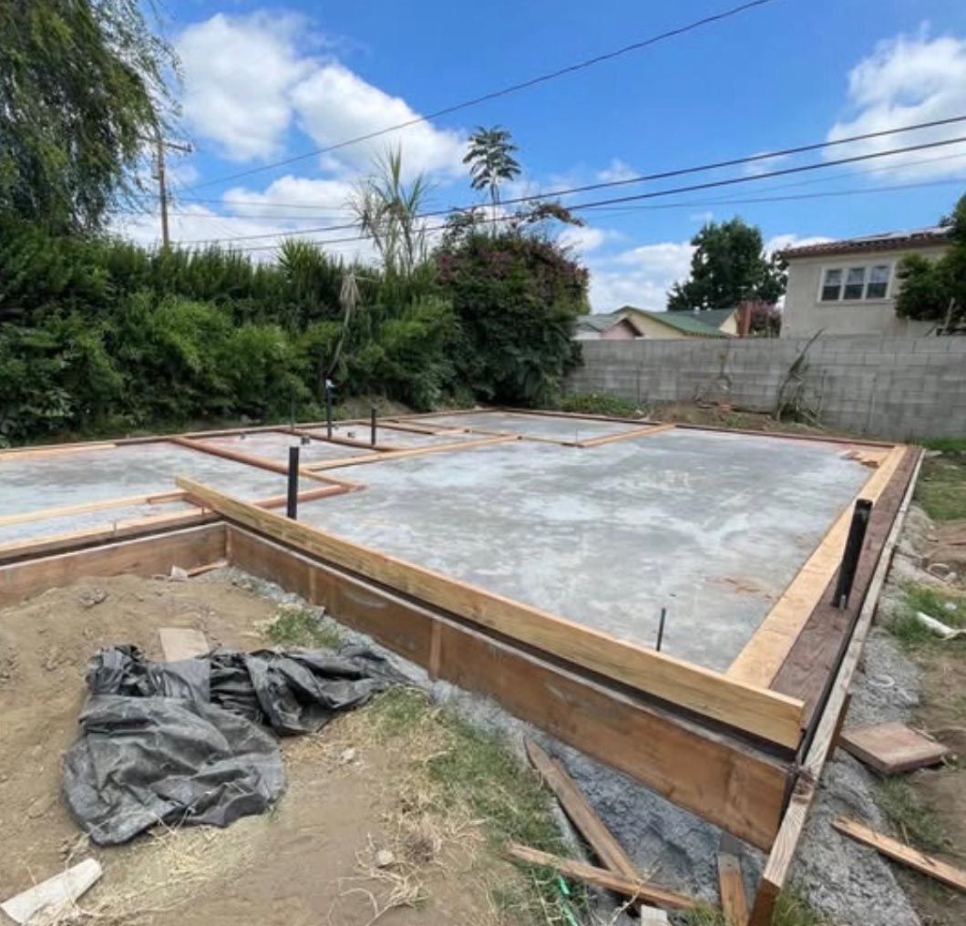 Freshly poured concrete foundation slab with wooden formwork in a backyard construction site