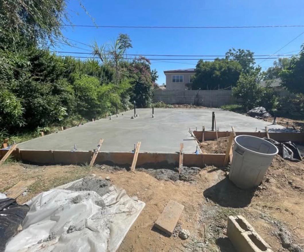 Fresh concrete slab foundation under construction in a sunny yard, with forms and materials around it