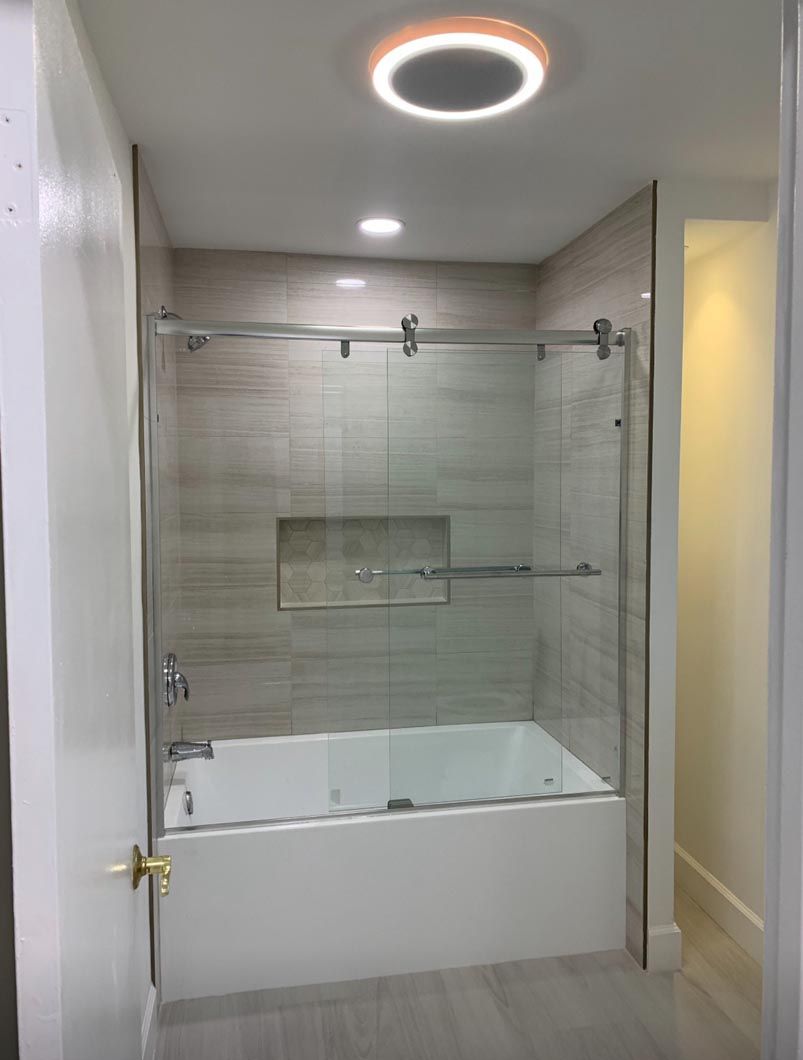 Modern bathroom with a white tub, glass shower enclosure, and round ceiling light.
