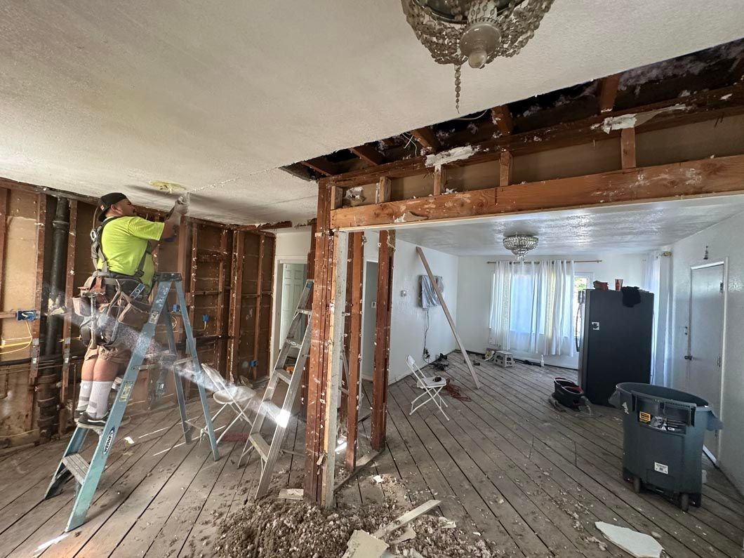 Worker in a bright vest renovating a room with exposed studs, debris, and construction tools.
