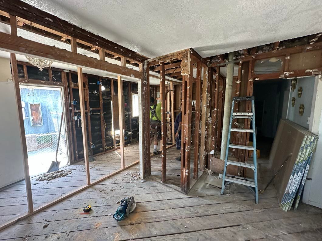 Interior of a room under renovation with exposed studs, debris on the floor, and a ladder near the wall