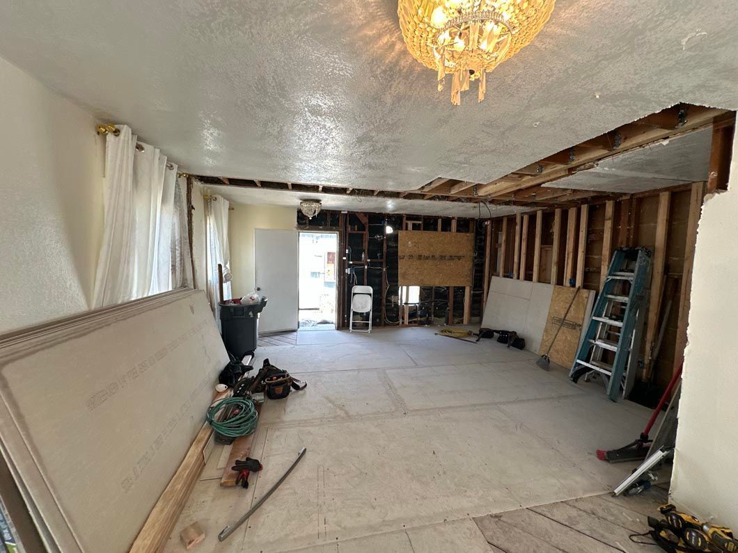 Renovation of a room with exposed studs, tools, ladder, and white protective floor covering