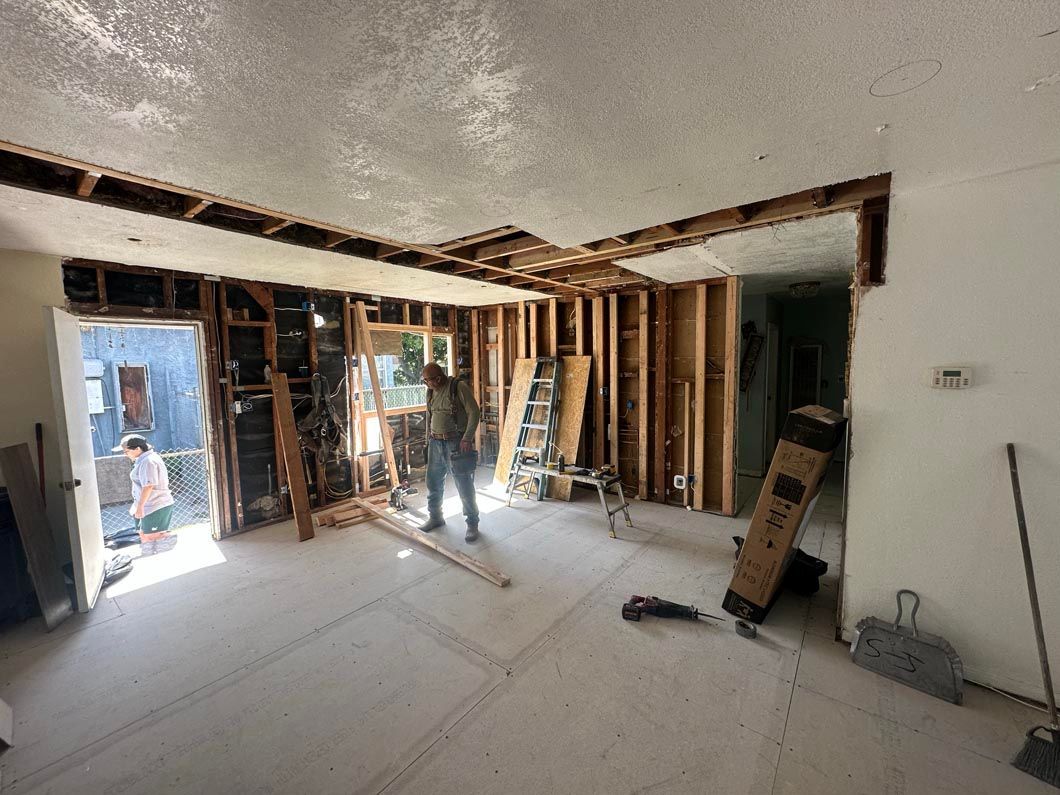 Interior under renovation with exposed studs, ladders, and construction materials scattered across the room