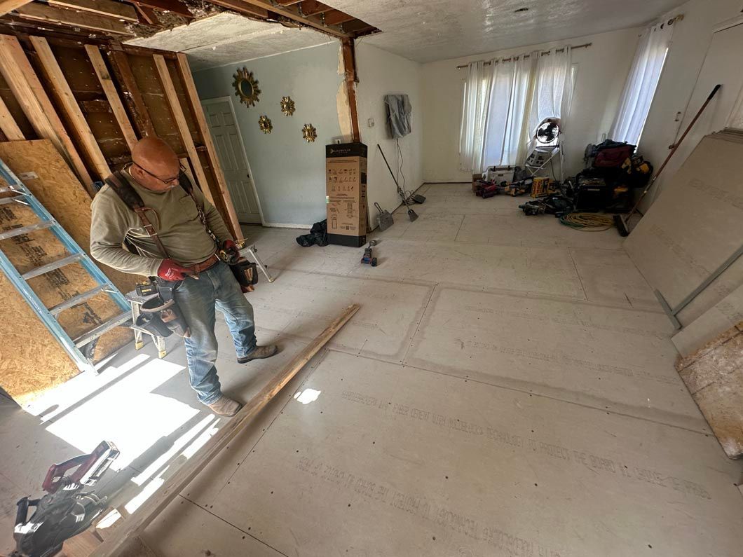 Worker with tools in a bright unfinished room, installing flooring beside a staircase.