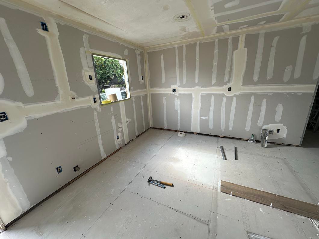 Empty drywall room under renovation with white walls, ceiling, and a window letting in daylight