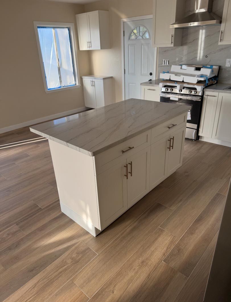 Modern kitchen with a central island, wood floors, white cabinets, and stainless steel appliances.