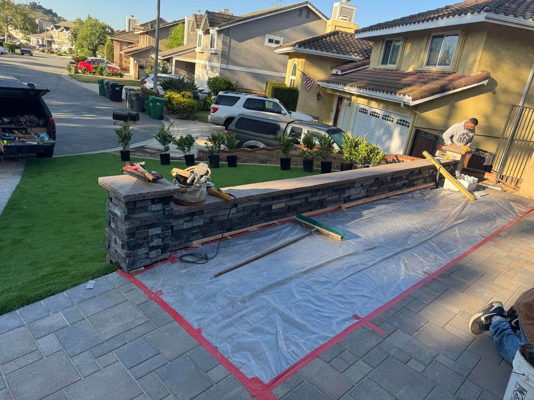 Marked driveway ramp under construction beside a suburban house, with red tape and stone retaining wall.