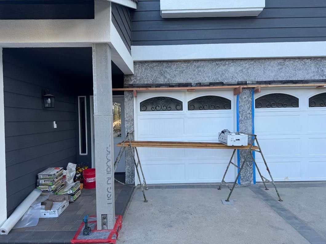 Exterior of a house under construction with garage doors, scaffolding, and building materials on the driveway