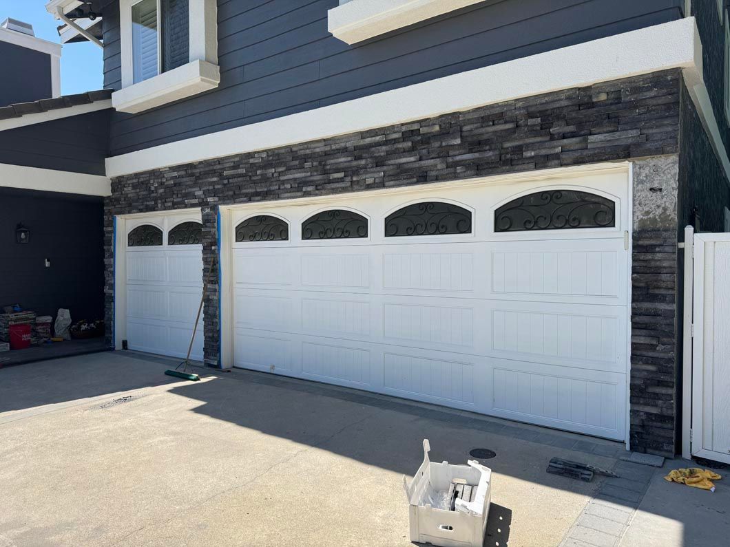 Modern house exterior with three white garage doors and stone trim in bright sunlight