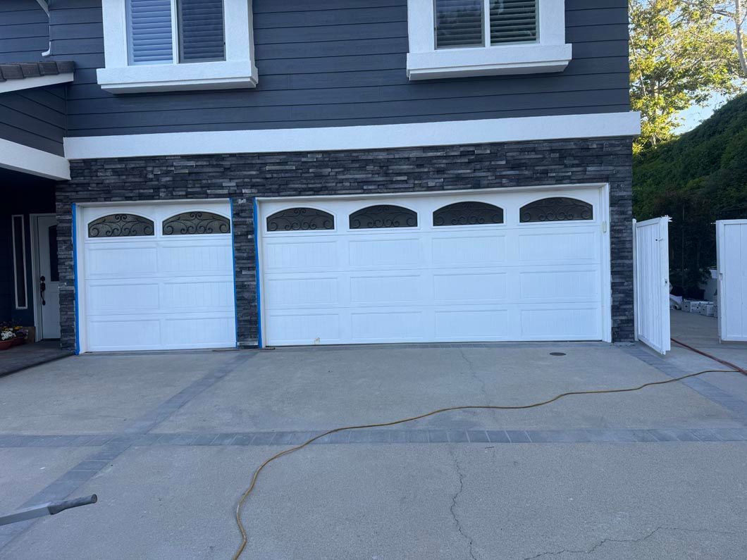 White three-car garage with decorative windows on a gray house exterior