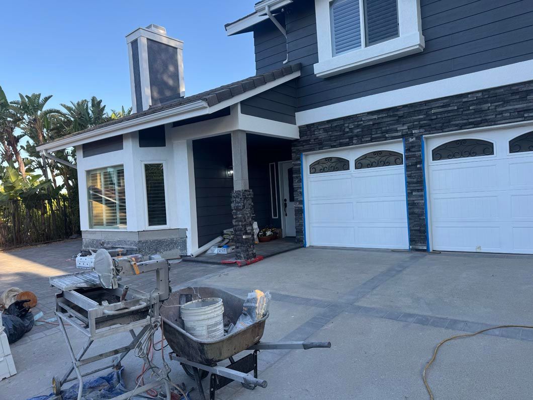 Suburban house exterior with blue siding, white garage doors, and construction tools on the driveway