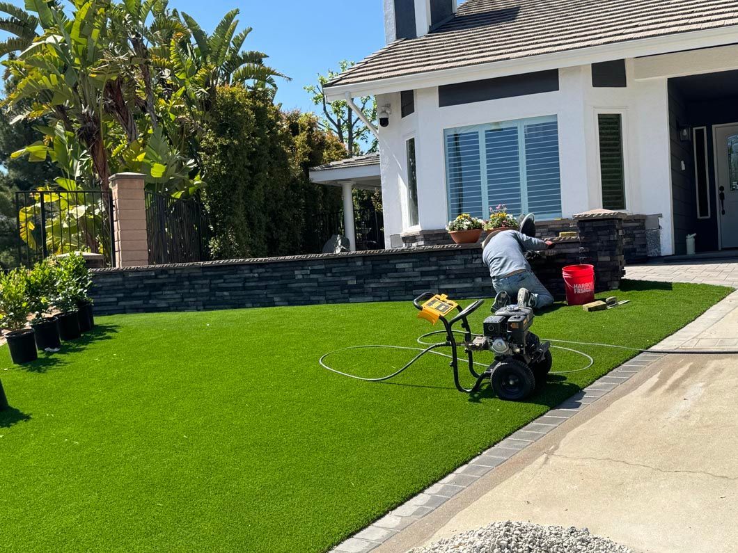 Person mowing a bright green lawn beside a striped house and concrete driveway.