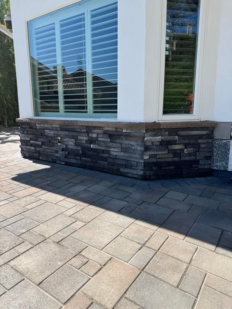 White building exterior with blue shutters, stone base, and paved walkway in bright sunlight