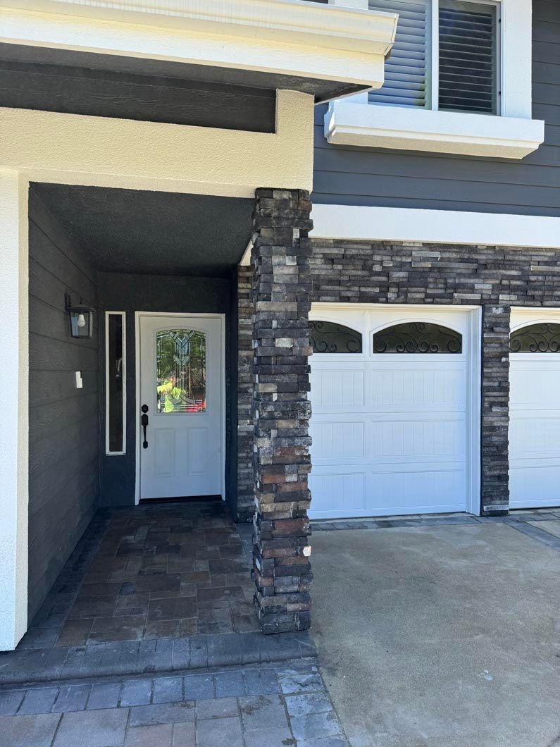 Front porch with stone columns, white front door, and attached garage on a suburban house.
