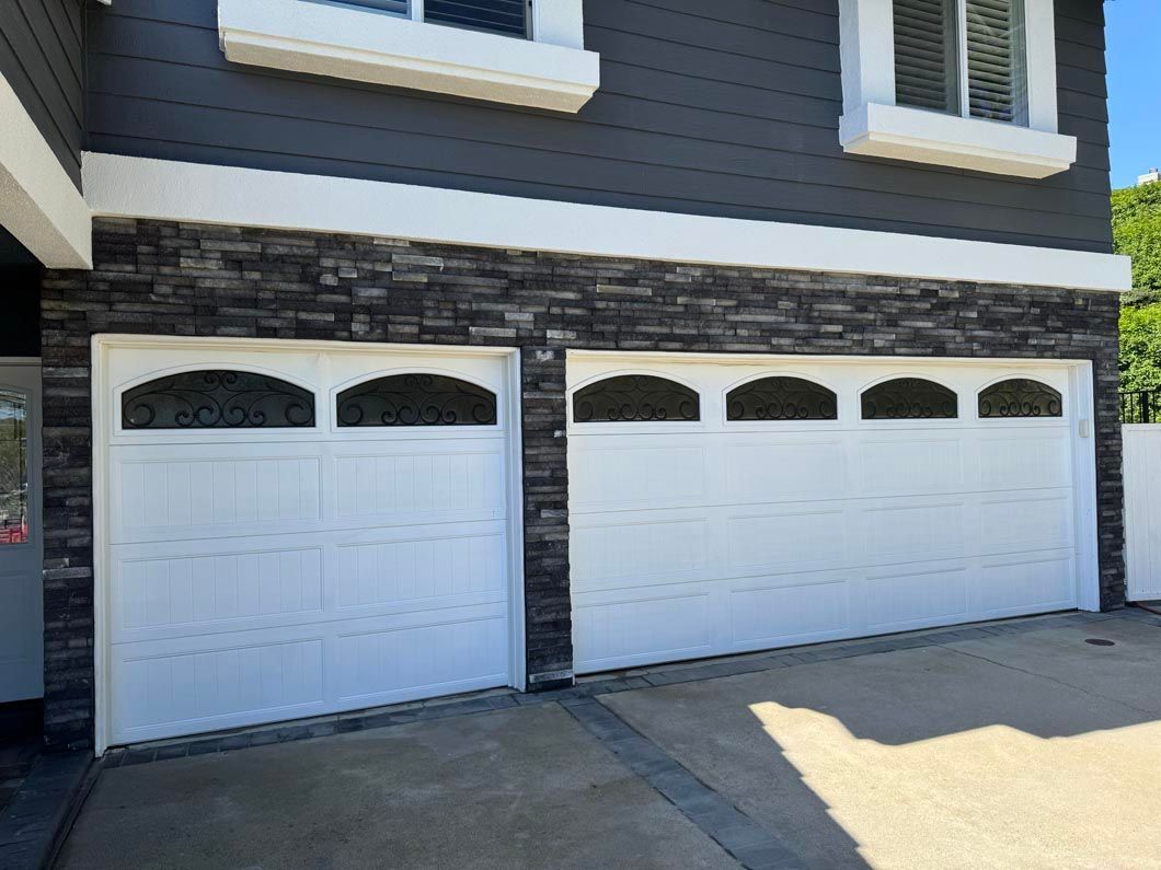Two white garage doors on a gray house with stone trim and a concrete driveway