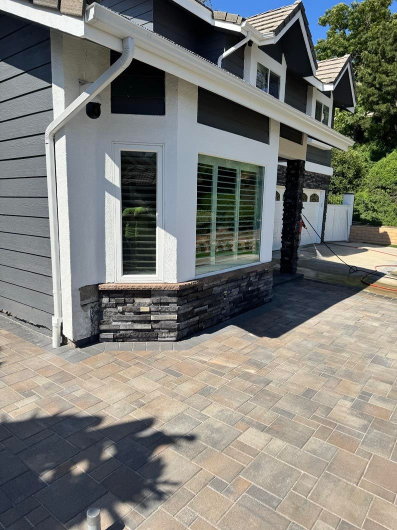 Modern house exterior with white trim, gray siding, stone base, and paved driveway in sunlight