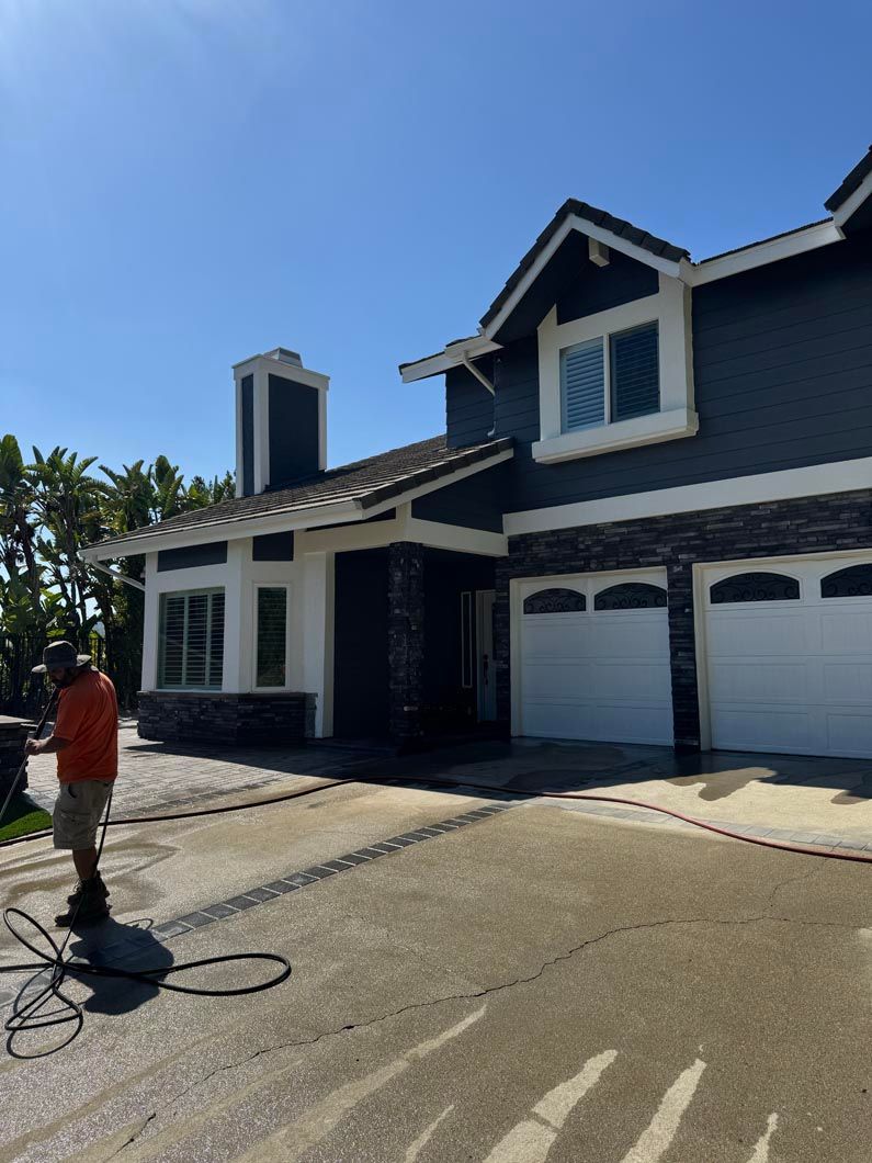 Two-story navy house with white trim and garage doors on a sunny day, person standing in the driveway
