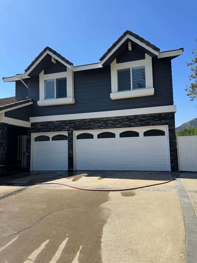 Two-story blue-gray house with white trim, four-car garage, and driveway under a clear blue sky