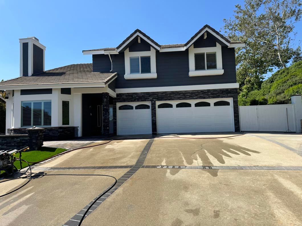 Two-story suburban house with white trim, dark siding, and a three-car garage under a clear blue sky