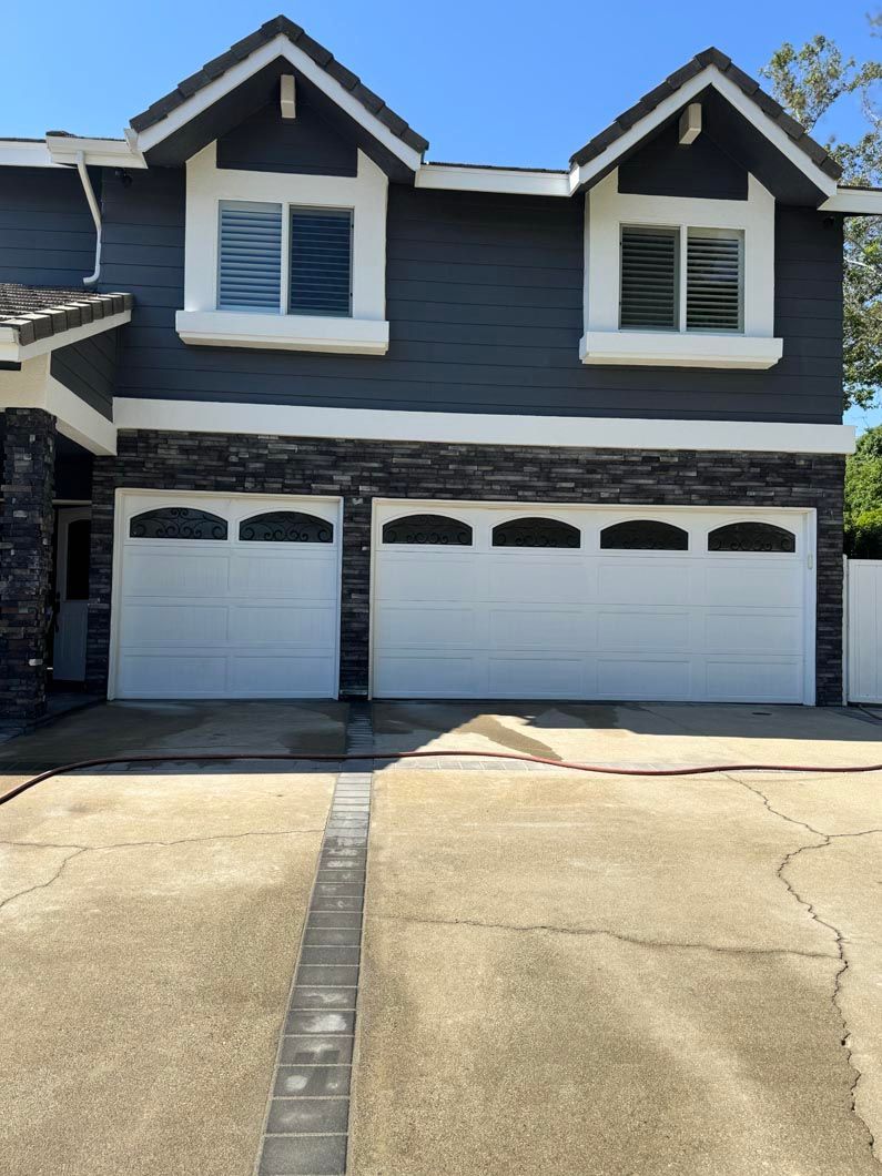 Two-story gray house with two white garage doors and a cracked concrete driveway
