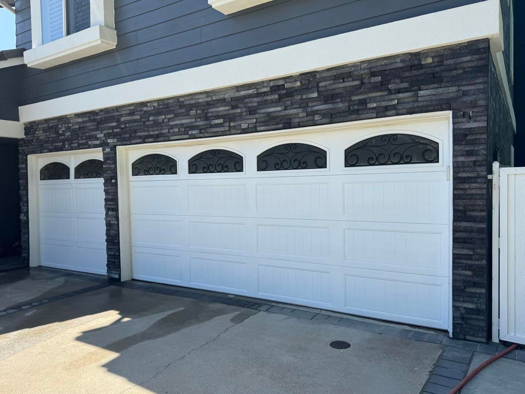 Three white garage doors on a house with stone trim and arched window panels