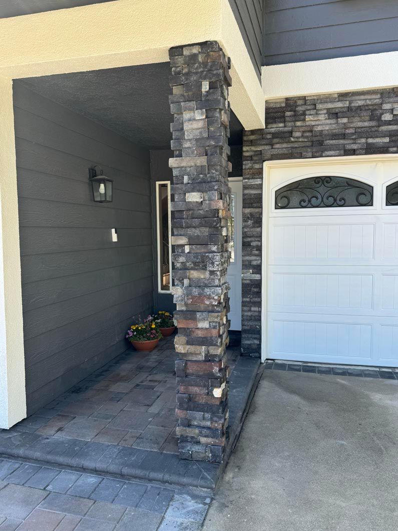 Front porch with stone column, gray siding, and a white garage door.