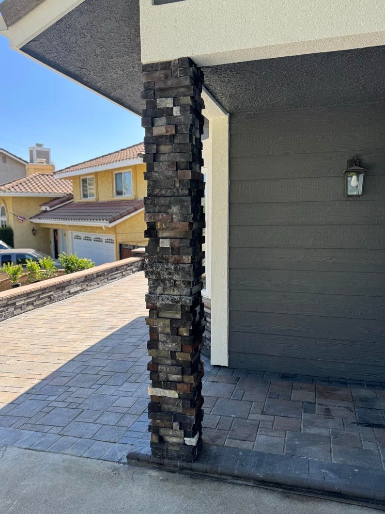 Stone column on a covered patio beside a driveway and neighboring house exterior