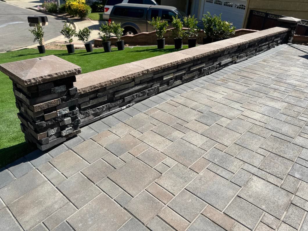 Stone retaining wall beside a paved driveway and landscaped lawn with shrubs and a parked SUV.